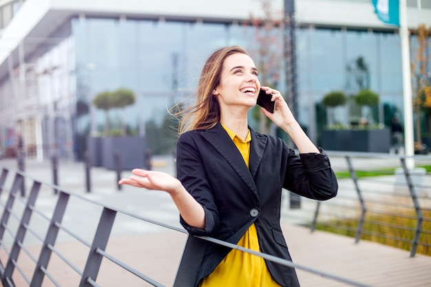 Onderneemster met een mobiele telefoon in de straat met bureaugebouwen