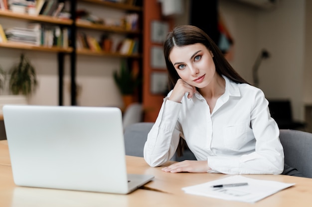 Onderneemster met laptop werkt bij bureau met documenten