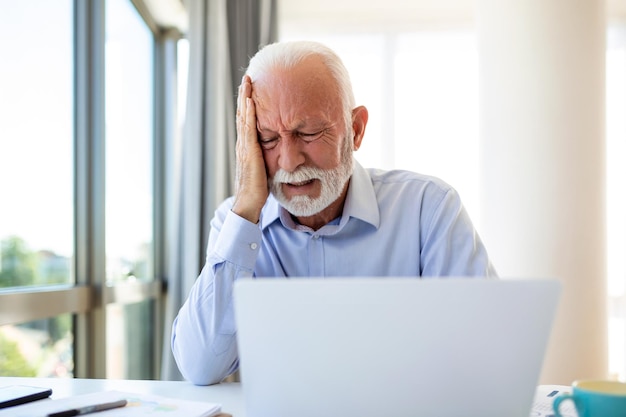 Ondernemer die op kantoor werkt met hoofdpijn van het bureau en de hele dag zit en werkt met een laptop of notebook die hoofdpijn heeft zieke werknemer die overwerkt