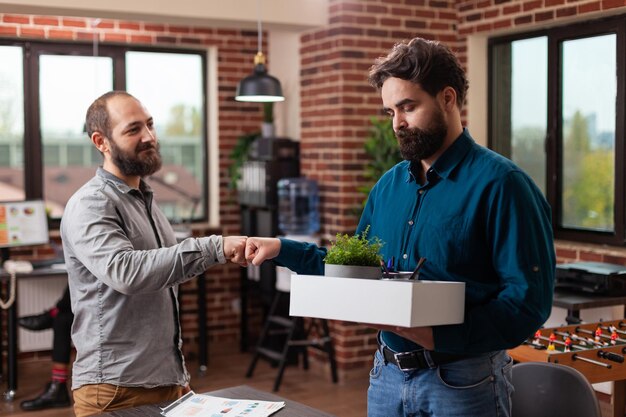 Foto ondernemer die vuist slaat met ontslagen trieste freelancer-man terwijl hij zijn pakket met bezittingen draagt na te zijn ontslagen. diverse zakenmensen die werken aan de bedrijfsstrategie in een startup-kantoor