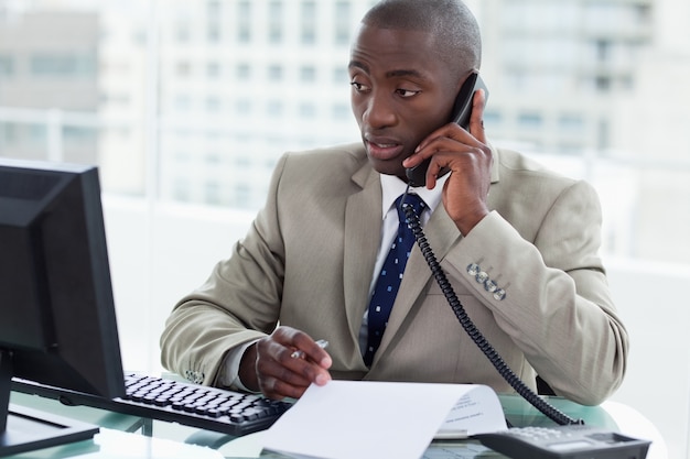 Ondernemer een telefoongesprek voeren terwijl hij naar zijn computer kijkt