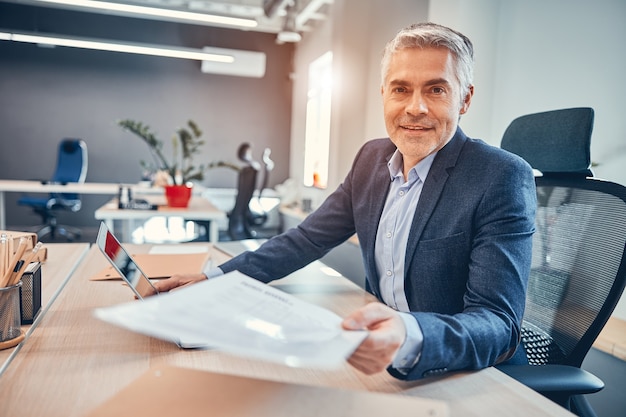 Ondernemer van bedrijf zittend op de stoel aan zijn bureau en het geven van een document