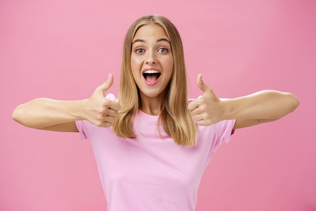 Ondersteunend meisje duimen opdagen met gelukkige positieve glimlach goedkeuring geven tegen roze achtergrond