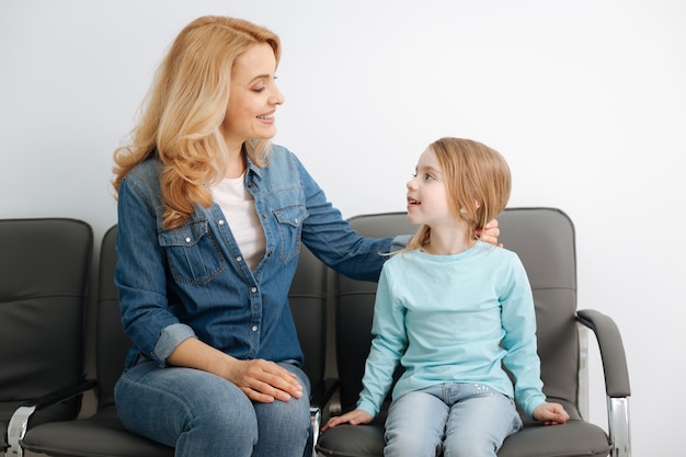 Ondersteunende, liefdevolle, zachte moeder die met haar kind praat en haar haar fixeert terwijl ze haar afleidt van nerveuze gedachten voordat ze een dokter ontmoet