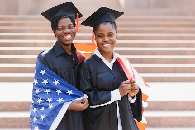 Onderwijs, afstuderen en mensenconcept - gelukkige internationale studenten in mortelborden en bachelorjurken met Amerikaanse vlag