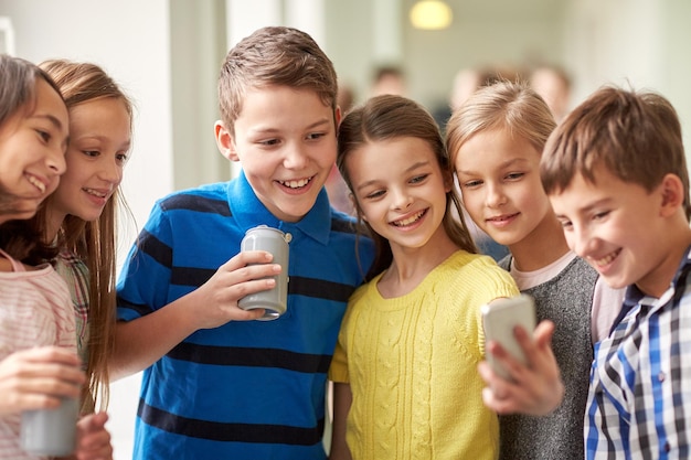 onderwijs, basisschool, drankjes, kinderen en mensen concept - groep schoolkinderen met smartphone en frisdrankblikjes die selfie in gang nemen