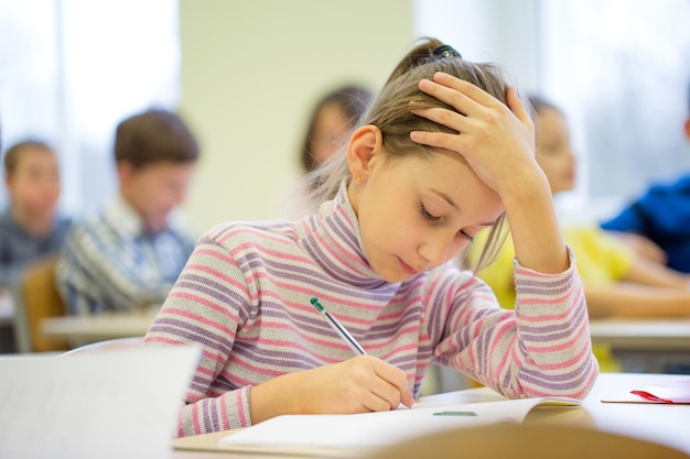 onderwijs, basisschool, leer- en mensenconcept - groep schoolkinderen met pennen en notitieboekjes schrijftest in de klas