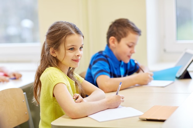 onderwijs, basisschool, leer- en mensenconcept - groep schoolkinderen met pennen en notitieboekjes schrijftest in de klas