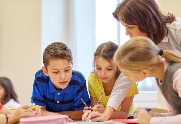 onderwijs, basisschool, leer- en mensenconcept - leraar die schoolkinderen helpt bij het schrijven van een test in de klas