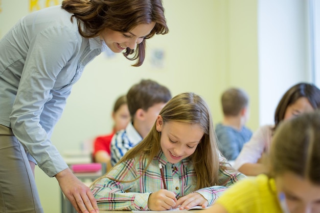 Foto onderwijs, basisschool, leer- en mensenconcept - leraar helpt schoolmeisje schrijftest in de klas