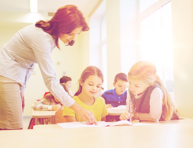 onderwijs, basisschool, leren en mensen concept - leraar helpt schoolkinderen in de klas