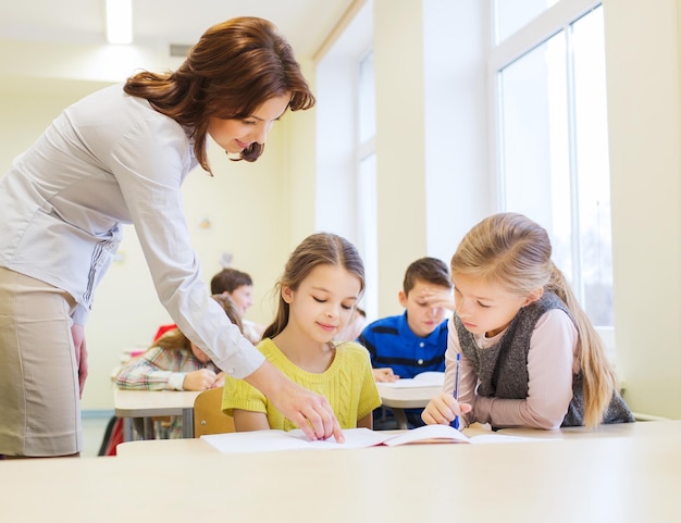 onderwijs, basisschool, leren en mensen concept - leraar helpt schoolkinderen in de klas