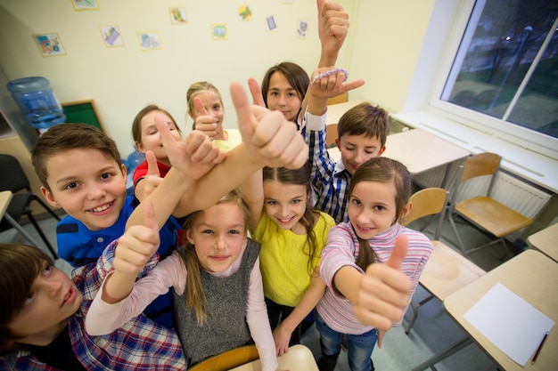 onderwijs, basisschool, leren, gebaar en mensenconcept - groep schoolkinderen en duimen opdagen in de klas