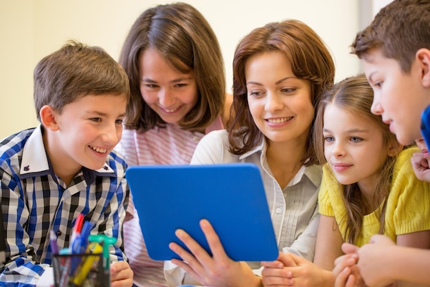 onderwijs, basisschool, leren, technologie en mensen concept - groep schoolkinderen met leraar op zoek naar tablet pc-computer in de klas