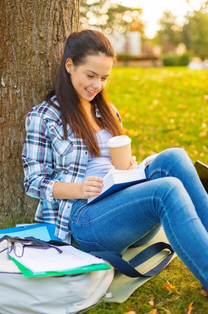 onderwijs, campus en mensenconcept - glimlachend tienerleesboek met koffie om mee te nemen