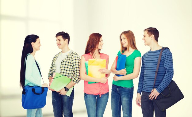 Onderwijs en mensenconcept - groep glimlachende studenten met tassen en mappen die discussie hebben