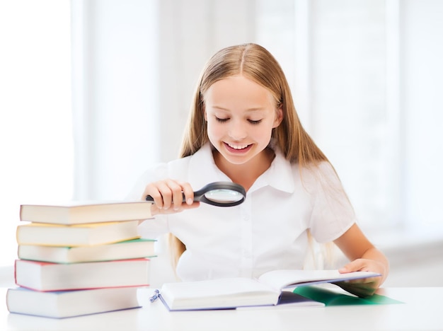 onderwijs en schoolconcept - klein studentenmeisje dat boek leest met vergrootglas op school