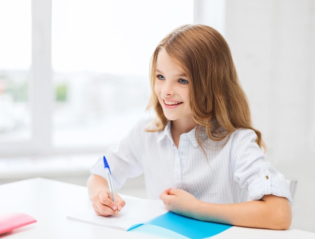 onderwijs en schoolconcept - klein studentenmeisje dat in notitieboekje op school schrijft