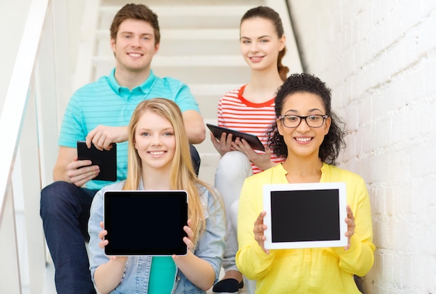 onderwijs en technologieconcept - glimlachende studenten die het lege scherm van de tabletpc computer tonen en op trap zitten