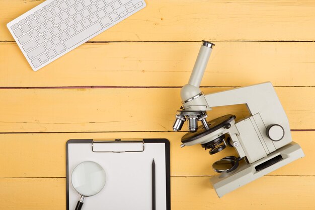 Onderwijs en wetenschap concept microscoop vergrootglas leeg klembord computertoetsenbord op het gele bureau