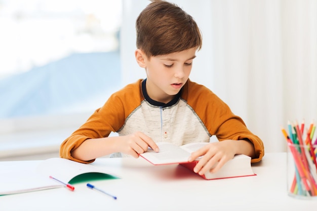 Onderwijs, jeugd, mensen, huiswerk en schoolconcept - studentenjongen leesboek of leerboek thuis