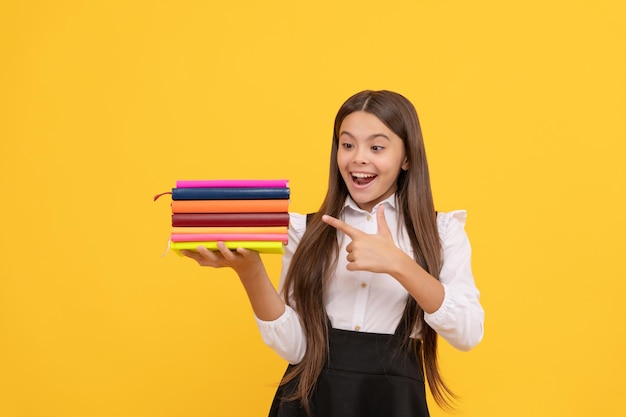 onderwijs. kinderboeken. overweldigd intellectueel kind. educatieve literatuur. boekenwijs kind. reclame. gelukkig tienermeisje wijzende vinger op boekstapel. te veel werk. terug naar school.