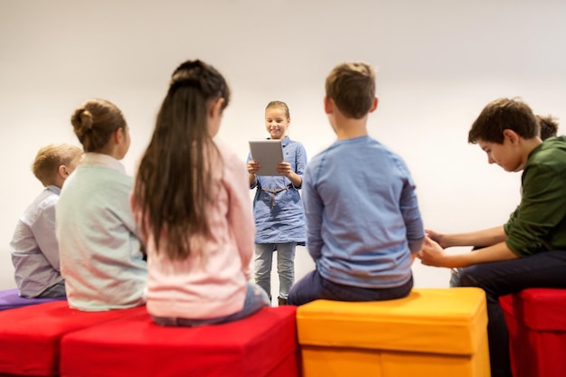 onderwijs, kinderen, leren, technologie en mensenconcept - gelukkig meisje met tablet pc-computer die iets presenteert aan een groep kinderen op school