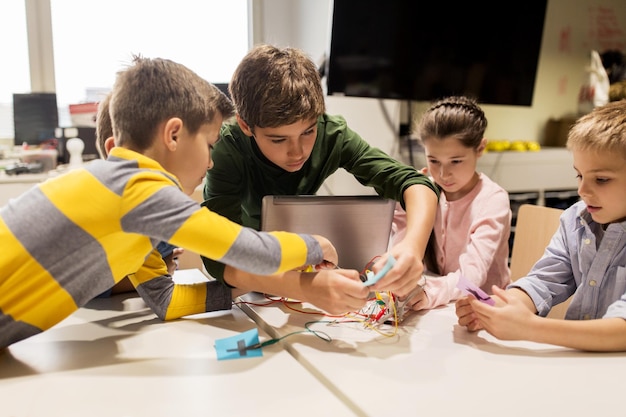 onderwijs, kinderen, technologie, wetenschap en mensenconcept - groep gelukkige kinderen met laptopcomputer spelen en uitvindingspakket bij robotica schoolles