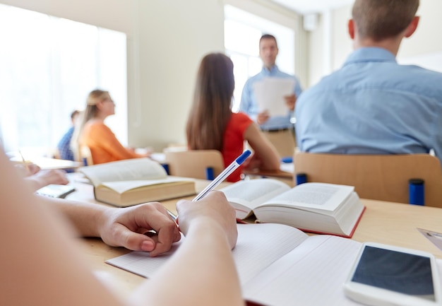 onderwijs, middelbare school, leren, technologie en mensenconcept - close-up van studentenhanden die naar notitieboekje en smartphone op bureau schrijven