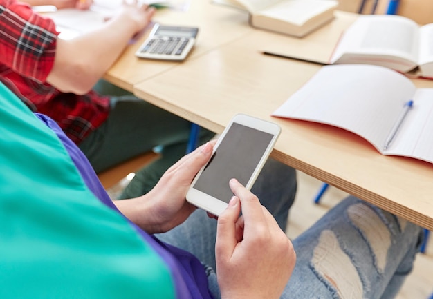 Foto onderwijs, middelbare school, leren, technologie en mensenconcept - studentenmeisje met smartphone sms'en op les