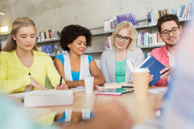 Foto onderwijs, middelbare school, mensen en leerconcept - groep internationale studenten aan tafel zitten met tablet-pc, boeken en notitieboekjes in de universiteitsbibliotheek van bovenaf