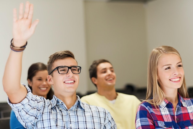 onderwijs, middelbare school, teamwerk en mensenconcept - groep glimlachende studenten die hand opsteken in collegezaal