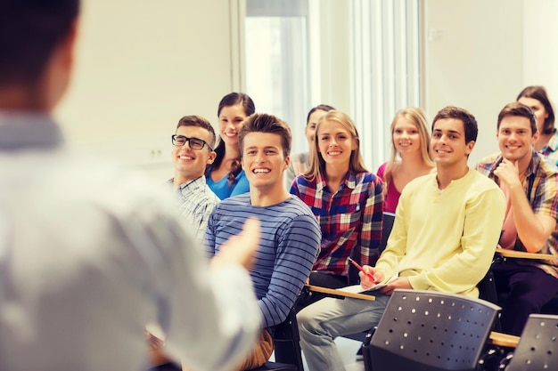 onderwijs, middelbare school, teamwerk en mensenconcept - groep glimlachende studenten met notitieboekjes en leraar in klaslokaal