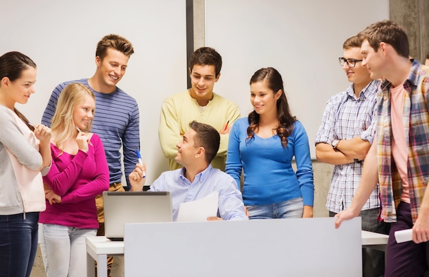 onderwijs, middelbare school, technologie en mensen concept - groep lachende studenten en leraar met papieren, laptopcomputer in de klas