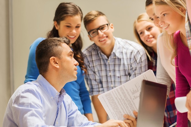 onderwijs, middelbare school, technologie en mensen concept - groep lachende studenten en leraar met papieren, laptopcomputer in de klas