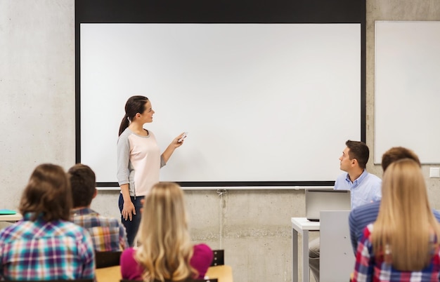 onderwijs, middelbare school, technologie en mensen concept - lachende student meisje met afstandsbediening, laptopcomputer staan voor whiteboard en leraar in de klas