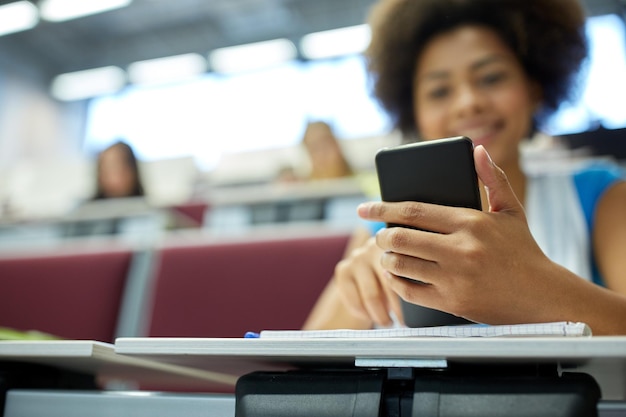 onderwijs, middelbare school, universiteit, leren en mensen concept - close-up van gelukkig Afrikaans studentenmeisje met smartphone in collegezaal