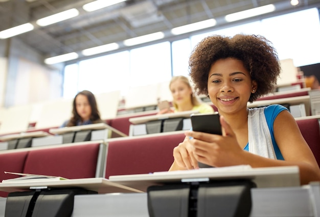 onderwijs, middelbare school, universiteit, leren en mensenconcept - afrikaans studentenmeisje met smartphone tijdens de lezing