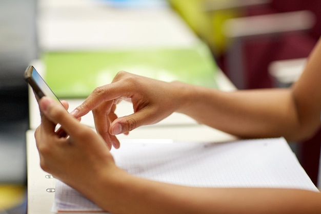 Foto onderwijs, middelbare school, universiteit, leren en mensenconcept - close-up van afrikaanse studentenmeisjeshanden met smartphone op lezing