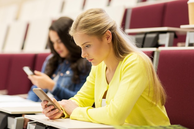 Foto onderwijs, middelbare school, universiteit, leren en mensenconcept - studentenmeisjes met smartphones op lezing