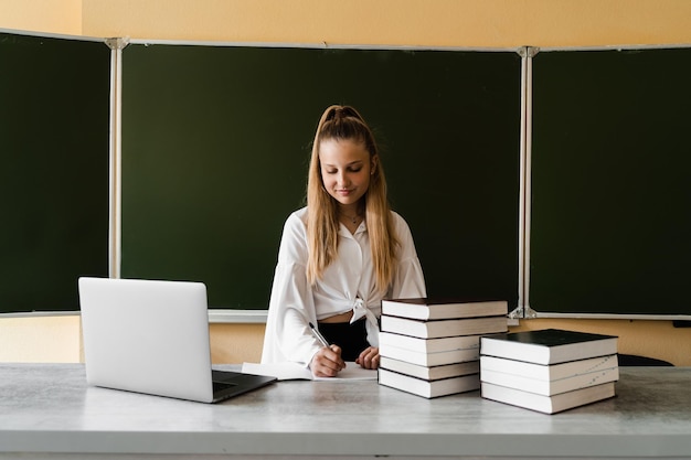 Onderwijs op school Schoolmeisje met laptop en boeken die huiswerk maken Meisje op schoolbestuur studeren en notities schrijven in notitieboekje