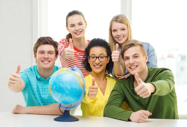 Foto onderwijs, reizen en aardrijkskunde concept - vijf lachende student met earth globe op school duimen opdagen