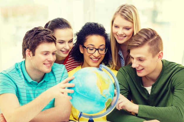 Foto onderwijs, reizen en aardrijkskunde concept - vijf lachende studenten kijken naar de aardbol op school