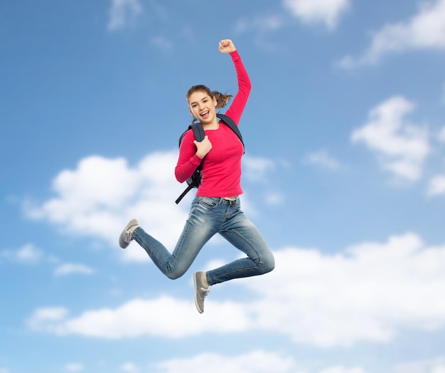 Foto onderwijs, reizen, toerisme, beweging en mensen concept - lachende jonge vrouw of student met rugzak springen in de lucht over blauwe hemelachtergrond