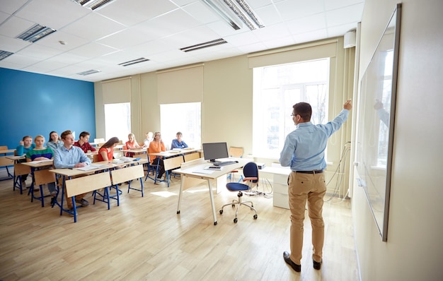 onderwijs, school, leren, onderwijzen en mensen concept - leraar staat voor studenten en laat iets zien op een wit bord in de klas