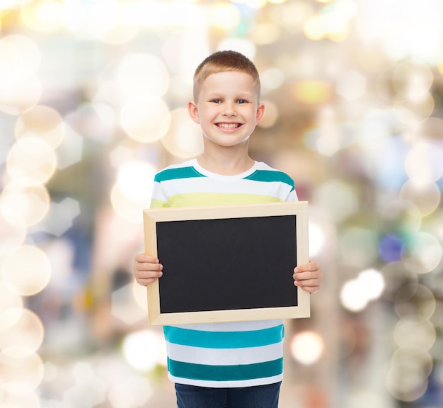 onderwijs, school, reclame en mensenconcept - glimlachende kleine jongen die leeg zwart bord over fonkelende achtergrond houdt