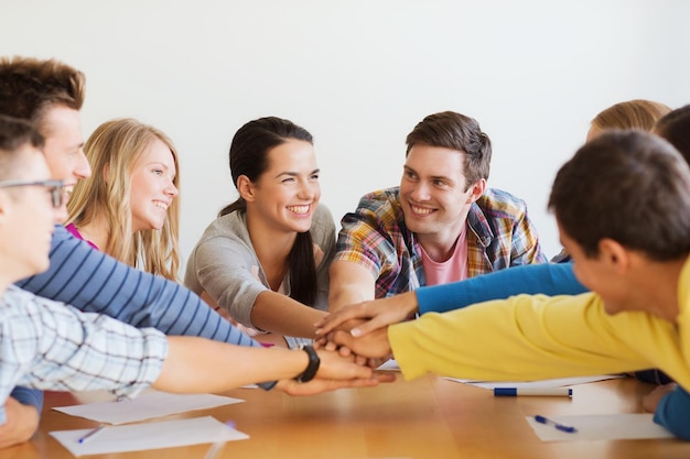 Foto onderwijs, teamwork en mensenconcept - lachende studenten met papieren die de handen op elkaar leggen