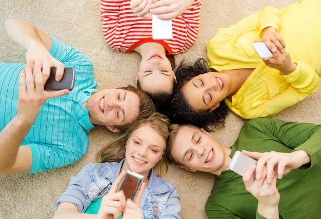 Foto onderwijs, technologie en geluk concept - groep jonge lachende mensen liggend op de vloer in cirkel met smartphones