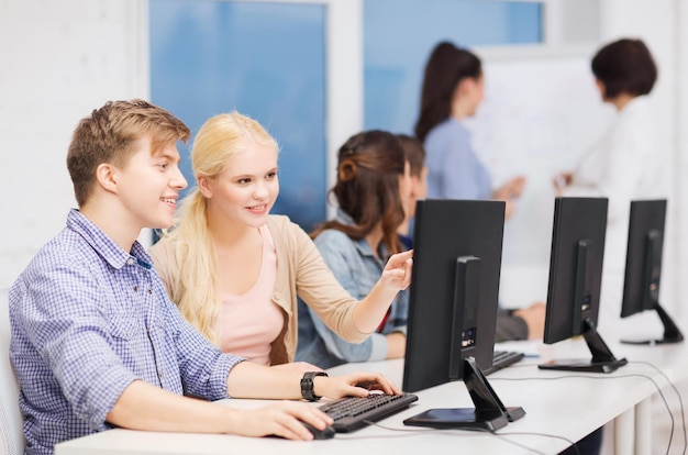 onderwijs, technologie en internet concept - groep lachende studenten met computermonitor kijken naar leraar op school