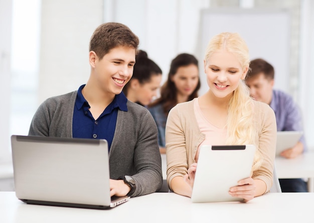 onderwijs, technologie en internet concept - twee lachende studentes met laptop en tablet pc op school